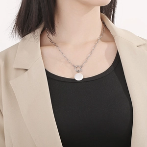 Close-up of silver-tone paperclip chain necklace with white round shell pendant on model