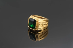 Macro detail of golden dragon ring with rectangular green emerald gemstone on black surface
