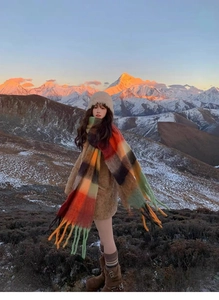 Detailed texture of thick rainbow plaid scarf with long tassels against a snowy mountain