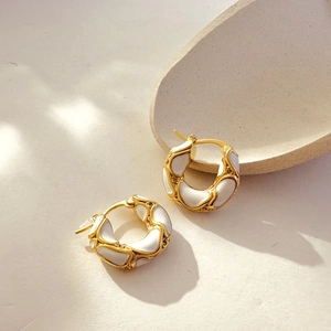 Detailed close-up of 18K gold hoop earrings with white enamel finish and wavy texture