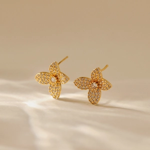 Elegant 18K gold leaf stud earrings paved with white zircons on cream fabric