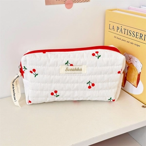 Close-up of cherry print quilted toiletry bag with golden logo and decorative ribbon