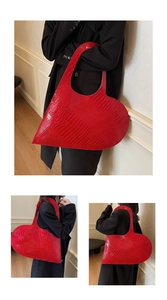 Detail view of large red heart-shaped tote bag with crocodile texture carried by model