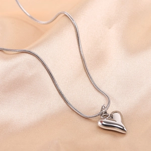 Detail of silver heart pendant on sleek snake chain over beige silk background