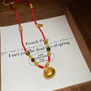Dettaglio della collana in corda rossa con pendente dorato Fu e perle occhio di tigre