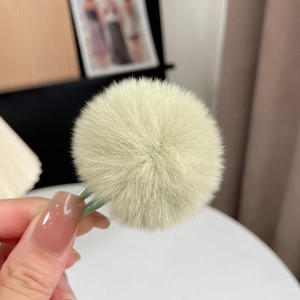 Close-up of a mini light green plush rabbit fur ball hair clip held by hand