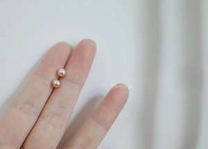 Macro detail of 925 silver pink pearl stud earrings held on fingertips for size
