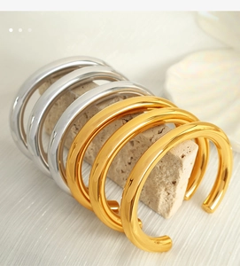 Minimalist C-shaped open bangles in gold and silver finish displayed on stone