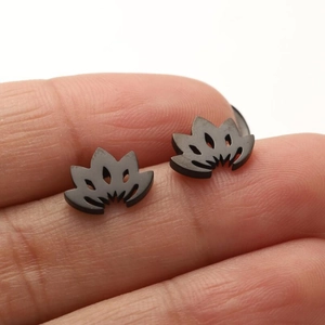 Close-up of matte black stainless steel lotus flower stud earrings held in fingers