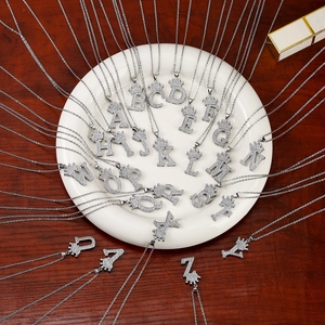 Detailed top view of 26 silver crown initial necklaces with crystals on a white plate
