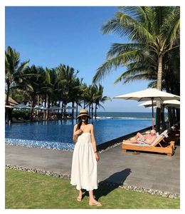 White sleeveless dress with wide-brim straw hat in a sunny tropical resort setting