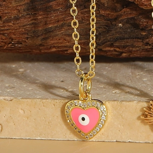 Detail of gold heart pendant with pink enamel, evil eye symbol, and zircon stones