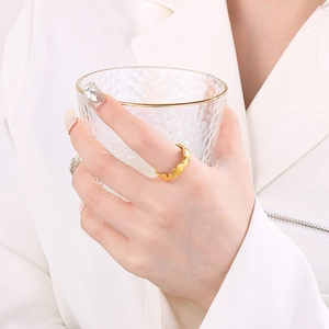 Close-up of a delicate gold heart-shaped ring worn while holding a textured glass