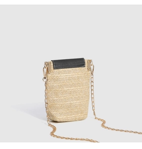 Close-up of straw woven texture with black leather flap and gold chain strap of beach bag
