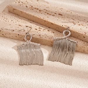 Macro detail of elegant silver metal tassel earrings on a textured stone surface