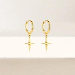 Close-up of golden four-pointed star pendant earrings on minimalist white background