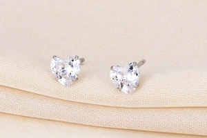 Close-up of heart-shaped zircon earrings on fabric, showing silver metal and fine cut