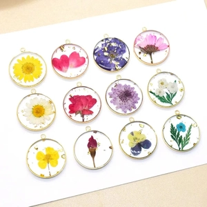 Flat lay of handmade resin pendants with dried daisy flowers and gold foil in copper frames