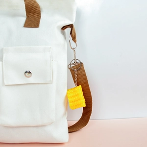 Realistic yellow PVC corn keychain with metal clasp hanging on a white canvas backpack