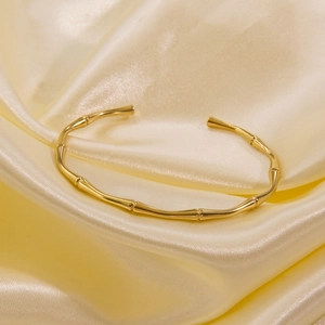 Detail of bamboo-style 14k gold plated stainless steel open bangle on silk background