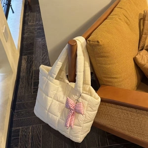 Quilted puffer tote bag in cream white with a checkered bow charm on a wooden chair