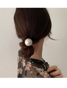 Dettaglio di un elastico con perla grande su uno chignon elegante castano scuro