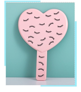 Detail of pink heart-shaped handheld mirror with black eyelash pattern on a blue background