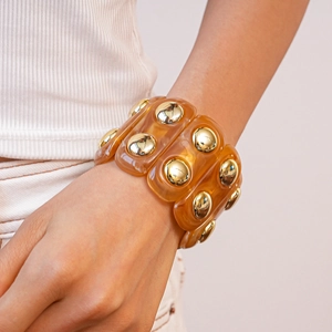 Macro detail of amber resin cuff bracelet with polished golden dome metal accents