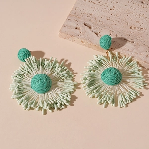 Detailed close-up of handmade green woven floral earrings on a travertine stone base