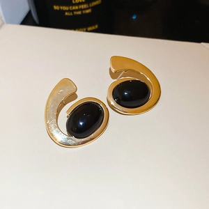 Macro shot of gold geometric earrings with oval black stones and spiral metal design