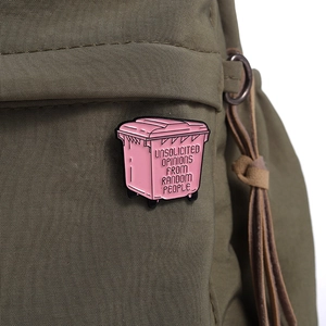 Close-up of a pink trash can enamel pin with sarcastic quote on green canvas bag