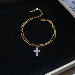 Macro detail of a double-layered gold bracelet with a sparkling zircon cross pendant