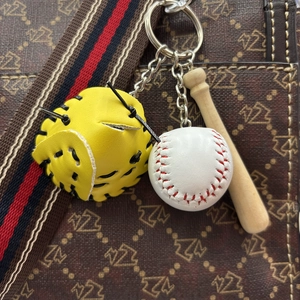 Close-up of a mini baseball keychain set with yellow glove and bat on a handbag