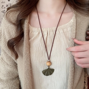 Close-up of ginkgo leaf pendant necklace with a wooden bead on a vintage cord