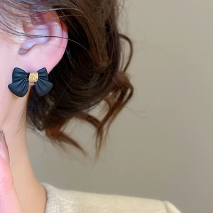 Close-up of black and gold bow earrings showing matte texture on the earlobe