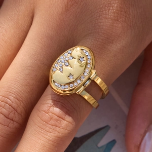 Macro detail of 18K gold-plated oval locket ring with star, moon and crystals