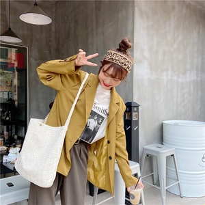 Street style shot of a woman wearing a yellow blazer with a white floral canvas crossbody bag