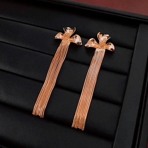 Close-up of rose gold flower tassel earrings with long metallic chains on a display tray