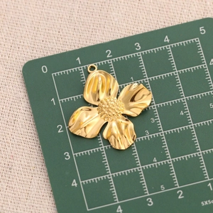 Macro detail of a 18k gold plated stainless steel floral pendant on a green grid mat