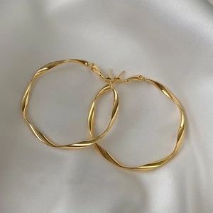 Elegant gold twisted geometric hoop earrings displayed on white satin fabric background