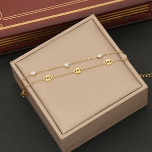 Detail of double-layer gold bracelet with evil eye and heart cubic zirconia charms