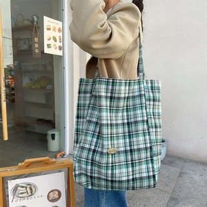 Detail of green and white checkered canvas tote bag showing the metallic logo and texture