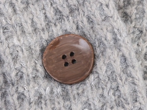 Macro shot of gray cashmere knit fabric with silver glitter silk and brown wooden button