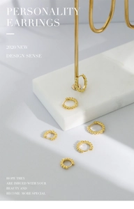 Close-up of golden hoop earrings with dotted texture on a white marble display stand