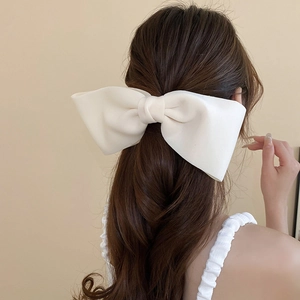 Detail view of a creamy white large fabric bow clip on brunette hair, elegant style