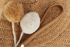 Detail of paper rope woven bag featuring khaki pom-poms and brown leather strap with metal stud