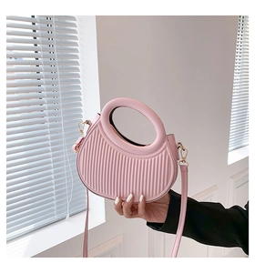 Detail of pink saddle bag with vertical pleats and golden hardware in natural light