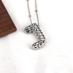 Macro shot of silver letter J pendant featuring a unique 3D faceted rivet texture and chain