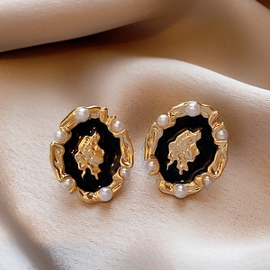Close-up of vintage gold earring with black enamel, pearl trim, and abstract face relief