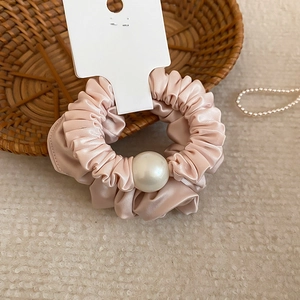 Vue détaillée d'un chouchou en satin rose champagne avec une grande perle blanche